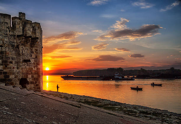 fisherman in sunset two boats and ancient tower background fisherman in sunset two boats and ancient tower background danube river stock pictures, royalty-free photos & images