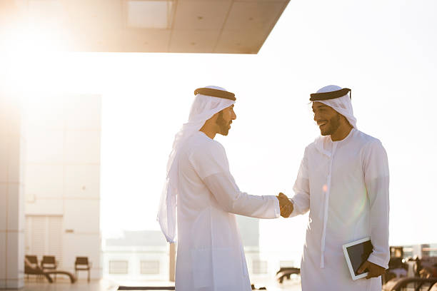 Two Arab Men Shaking Hands Two arab entrepreneurs doing business and shaking hands. One is holding a digital tablet. united arab emirates stock pictures, royalty-free photos & images