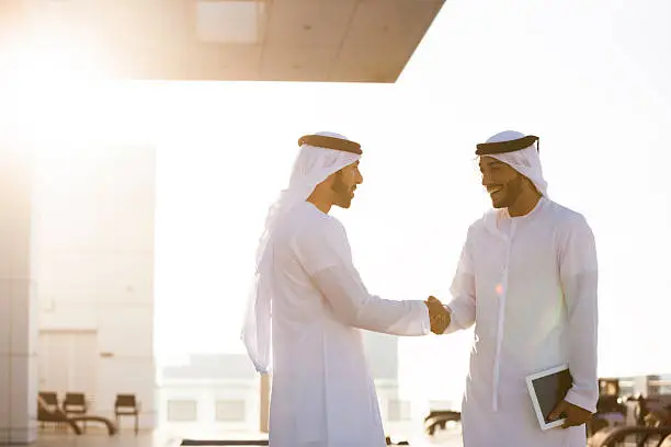 Two arab entrepreneurs doing business and shaking hands. One is holding a digital tablet.