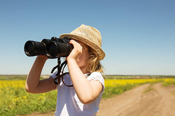 istock Little blonde girl in straw hat looking through binoculars outdo 483140912