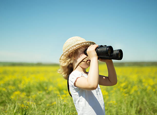 istock Little blonde girl in straw hat looking through binoculars outdo 483141784