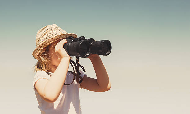 istock Little blonde girl in straw hat looking through binoculars outdo 483141830