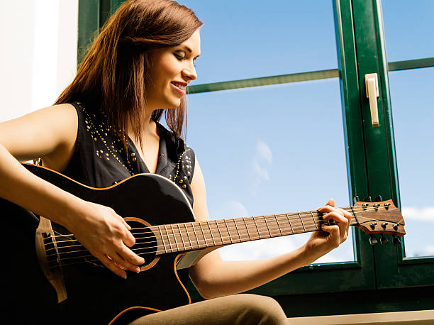 istock Smiling woman playing guitar by a window 483150605
