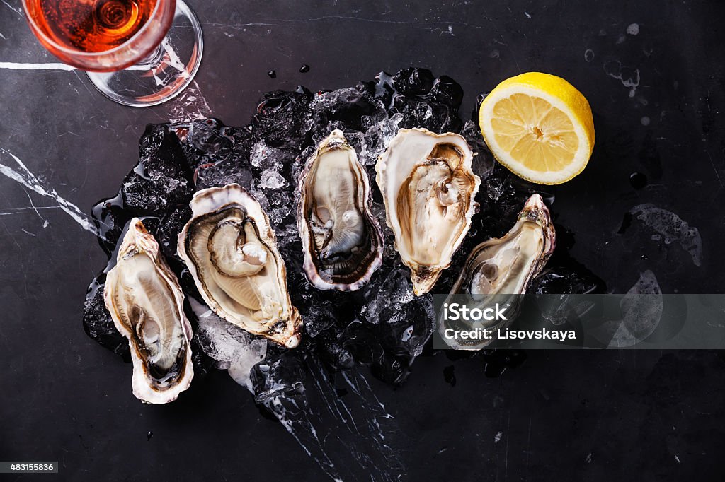 Opened Oysters with ice, lemon and wine Opened Oysters on dark marble background with ice, lemon and rose wine 2015 Stock Photo