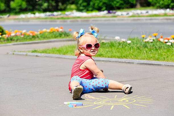 istock little girl drawing sun with chalks on a street 483156342