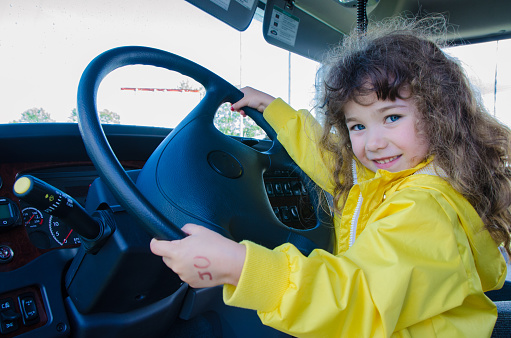Little girl sitting behing the steering wheel of a big truck and smiling at camera with pride