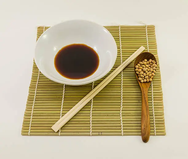 soysauce in white bowl with bamboo chopsticks and dried soybean in wood spoon