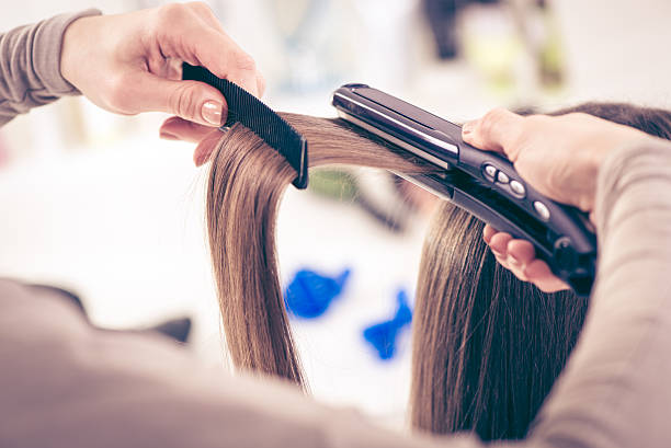 Hair Straighteners Close-up of a hairdresser straightening long brown hair with hair irons. straight-hair stock pictures, royalty-free photos & images
