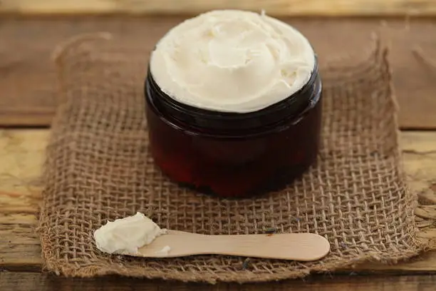 Jar of creamy body butter with wooden tester spoon on burlap