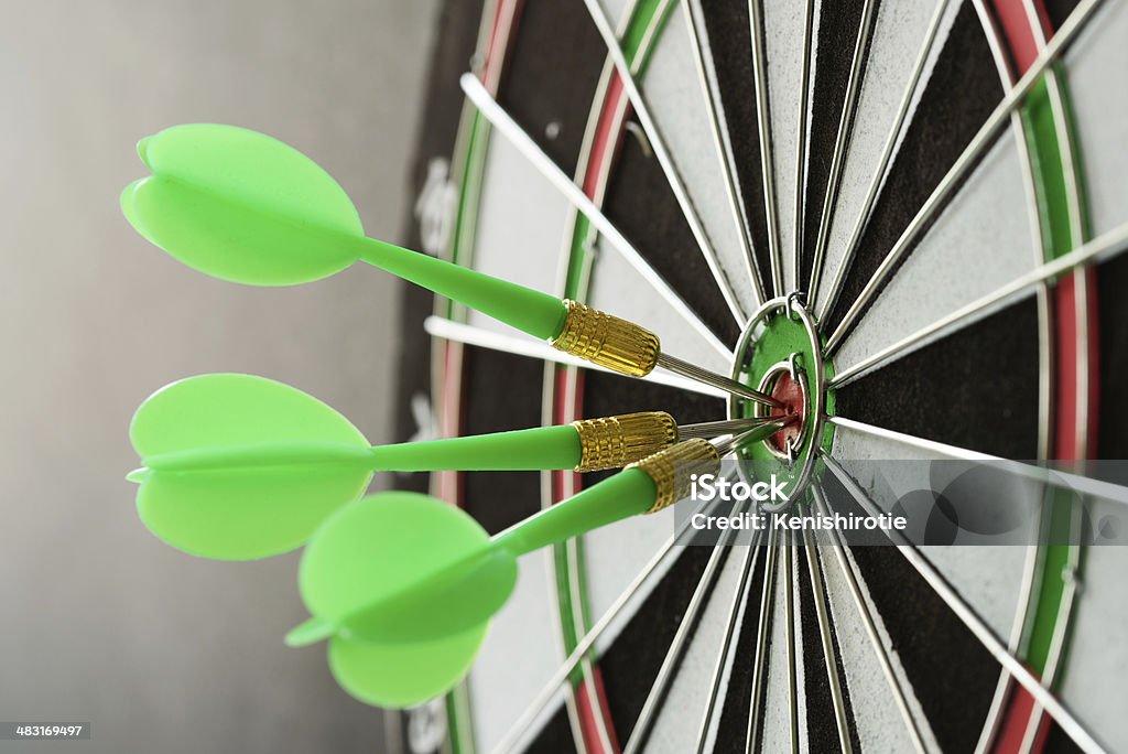 Consistency Three green darts pinned on the center of dartboard Three Objects Stock Photo