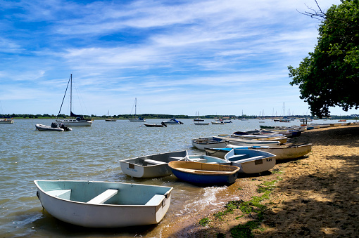 Waldringfield, Suffolk, England - June 15, 2015: Groups of rowing boats beside the River Deben at Waldringfield in Suffolk, eastern England on a sunny spring day, ready for their owners to row out to their yachts which are moored in the river. Waldringfield is a tiny but pretty village, popular with tourists and the sailing community.