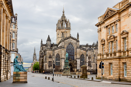 Edinburgh, United Kingdom - June 21, 2015: The St Giles Cathedral on Royal Mile, Edinburgh, United Kingdom. David Hume Statue is on the left. The Royal Mile is the name given to a succession of streets forming the main thoroughfare of the Old Town of the city of Edinburgh in Scotland. Tourists are walking around. Sky with clouds is in background.