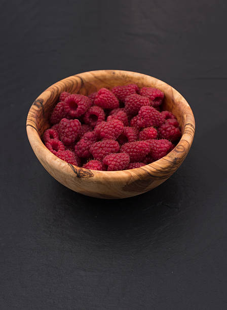 raspberries in a wooden bowl on black slate stone background