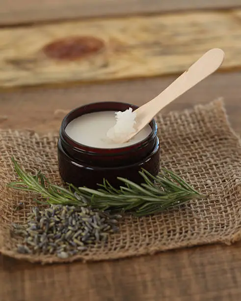 Jar of herbal salve or balm with wooden spoon, on burlap with lavender and rosemary for natural beauty.