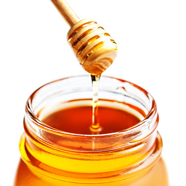 istock Dipping with honey in glass jar isolated on white 483180038