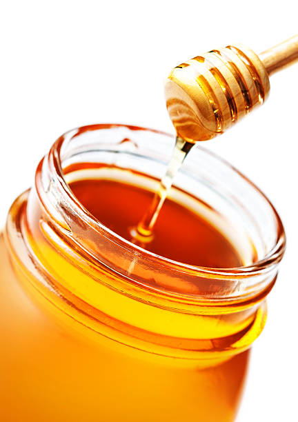 istock Dipping with honey in glass jar isolated on white 483180040