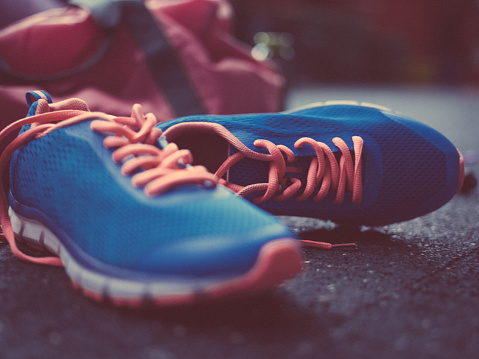 Closeup shot of colourful blue sneakers  with bright orange laces lying on a concrete floor in soft light in a gym with a gym bag in the background