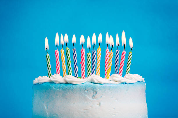 Birthday Cake A birthday cake with lighted candles against a blue background.  Focus is on the candles. birthday cake stock pictures, royalty-free photos & images