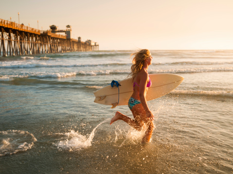 A women surfer running in the ocean at sunset.http://blog.michaelsvoboda.com/SurferGirlsBanner.JPG