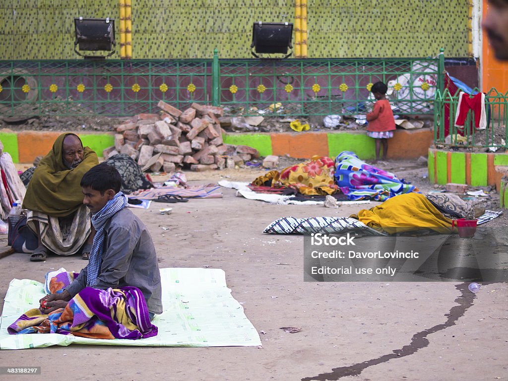 Sleep at Station Kolkata, India - January 4, 2014: People sleeping or sitting on the blanket while waiting for train in front of the Kolkata railway station. . In background is small girl plying in front of station wall. Asia Stock Photo