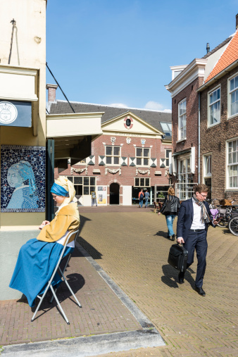 Delft, Netherlands - April 5, 2014: Girl acting in the role of the girl with the pearl earring, painted by Johannes Vermeer 17th century. Man passing with more intrst for his smartphone 
