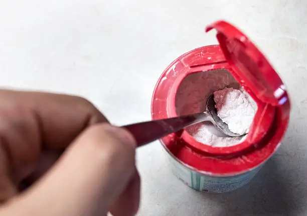 A teaspoon of baking powder/soda being taken from a container.