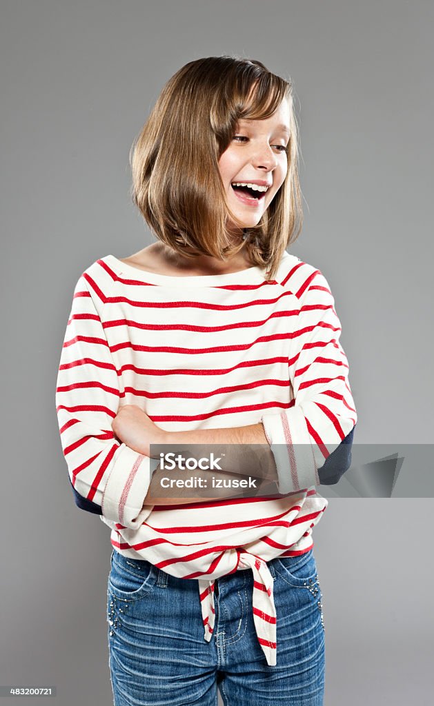 Cute girl Portrait of cute girl wearing striped blouse and jeans, standing against grey background with arms crossed and laughing, Studio shot. 10-11 Years Stock Photo