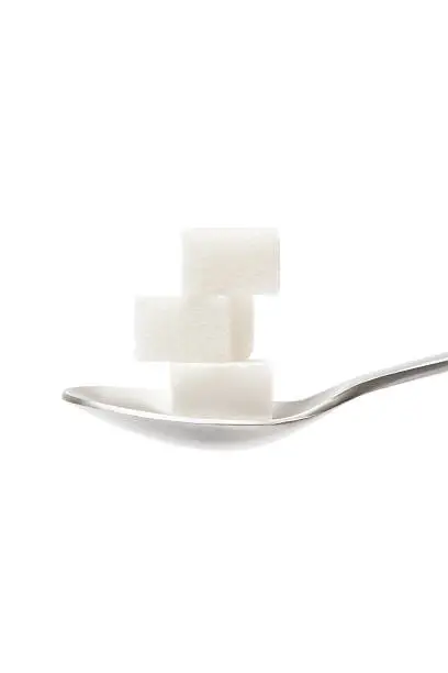 Stack of three sugar cubes on a silver teaspoon. Isolated on a white background.
