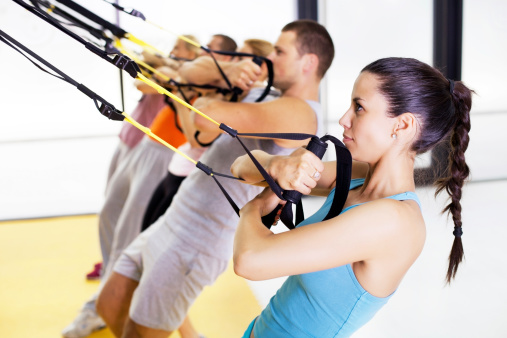 Group of people exercising with hanging fitness straps at the gym.