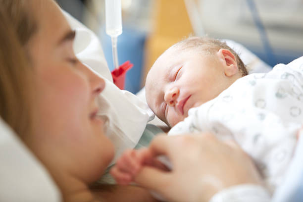 A beautiful 28 year old woman holding her sleeping 2 days old daughter. In a hospital scene
