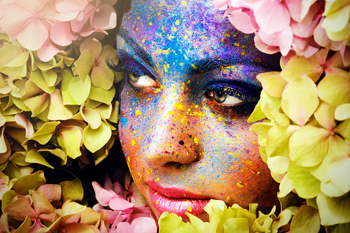 woman portrait with colorful face powder surrounded by  flowers.