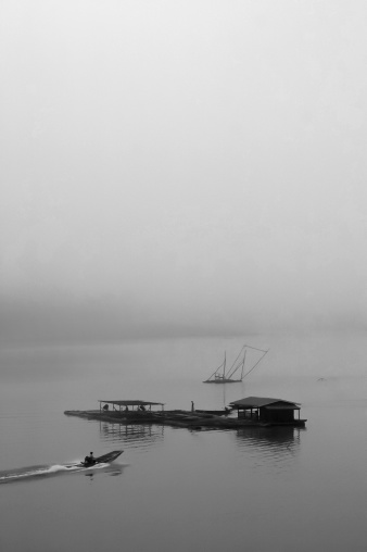 Sailing in the foggy morning in Sangkalaburi, Thailand. The boat driver is silhouette and unrecognisable.