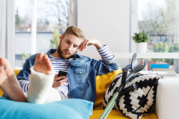 Young man with broken leg using smart phone at home Young man with broken leg in plaster cast lying down on sofa at home and using a smart phone. ankle photos stock pictures, royalty-free photos & images