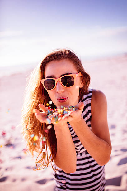 Young Woman blowing colorful confetti at the beach