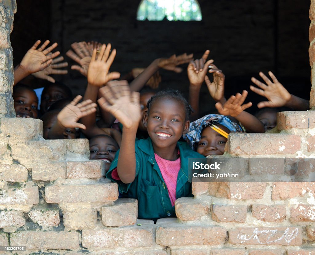 Several African children waving hands in Tchad A group of young children waving from inside of a student center in Tchad, Africa.  A smiling young girl wearing pink and blue waves along with several other boys and girls.  The children stand near an open window. Chad - Central Africa Stock Photo