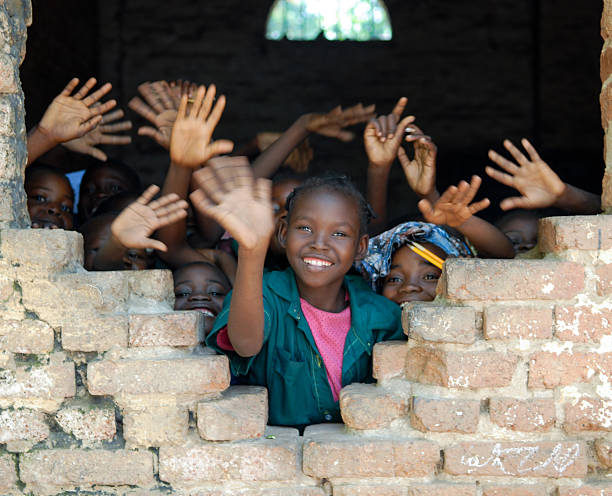 Several African children waving hands in Tchad A group of young children waving from inside of a student center in Tchad, Africa.  A smiling young girl wearing pink and blue waves along with several other boys and girls.  The children stand near an open window. central africa stock pictures, royalty-free photos & images