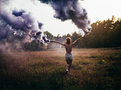 Hippie girl running through field with purple smoke flares