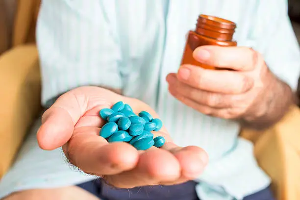closeup of an old caucasian man with a pile of blue pills in his hand