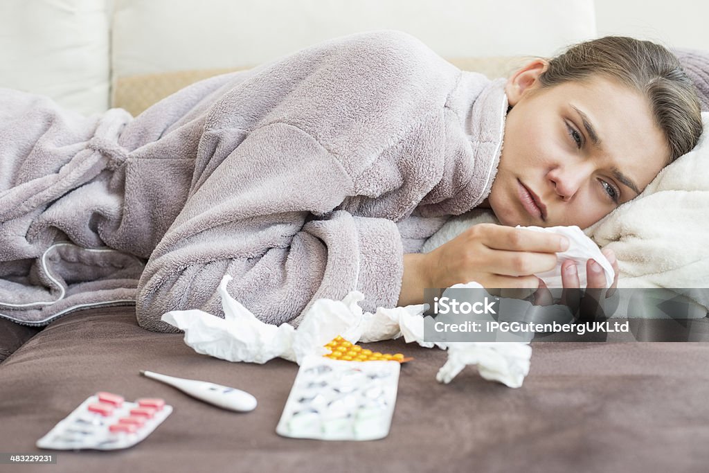 Sad woman with tissue and medicines lying on bed 20-24 Years Stock Photo