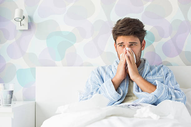 Sick man blowing his nose while sitting on bed Sick man blowing his nose while sitting on bed at home cold and flu man stock pictures, royalty-free photos & images