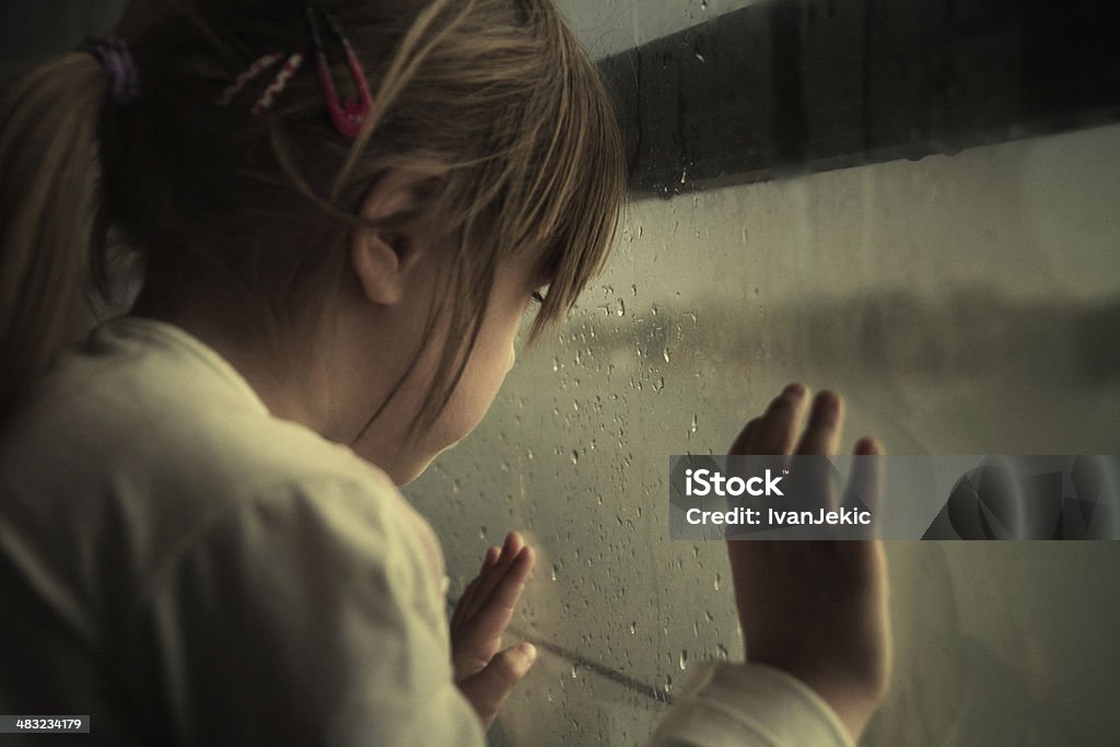 Lonely child looking through window Sad little girl looking through the rainy window. Grain added for texture. Child Stock Photo