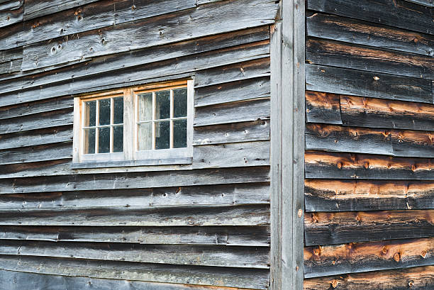 Corner Detail of Weathered Barn Walls with Two Windows and Rustic Gray and Brown Wood Siding.