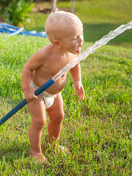 poco carino bambino ragazzo giocando con tubo flessibile in gomma - moisten foto e immagini stock