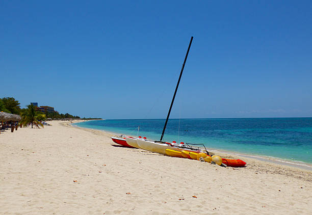 A vibrant catamaran rests on the pristine white sands of Grace Bay Beach in Providenciales, Turks and Caicos. The turquoise waters stretch to the horizon under a striking blue sky scattered with textured clouds, capturing the essence of a perfect Caribbean day.