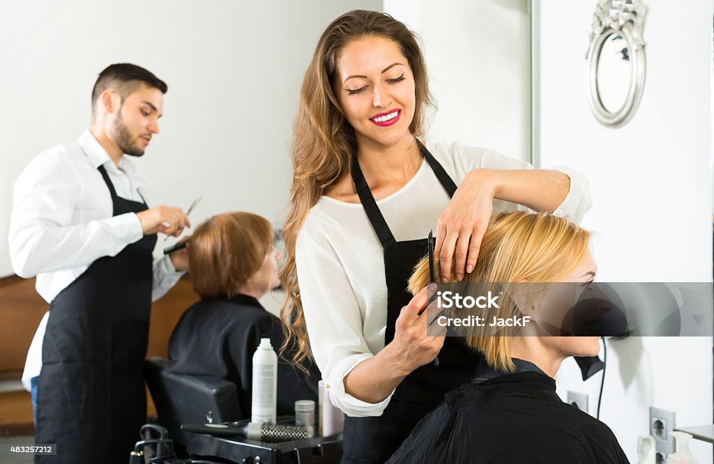 Happy client in a barbershop Smiling client sitting in a hair salon while hairdresser is combing her hair. Focus on client Hair Salon Stock Photo