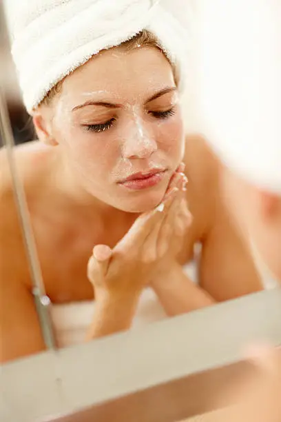 Reflection of a beautiful young female scrubbing and cleaning her face with soap in a mirror