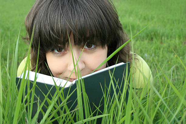 Pretty girl on a grass looking over the book stock photo