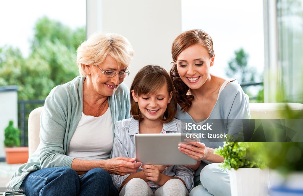 Three generation family with digital tablet Beautiful three women - daughter, mother and grandmother sitting on sofa at home and using a digital tablet together. Digital Tablet Stock Photo