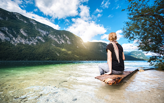 Young woman sitting on bench in the lake at famous Slovenian mountain lake (Bohinj Lake).