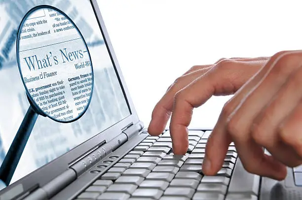 Photo of OnLine News, man's hands laptop keyboard, magnifying glass on screen